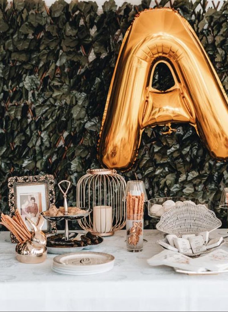 Gold letter balloon above a styled dessert table against a foliage wall